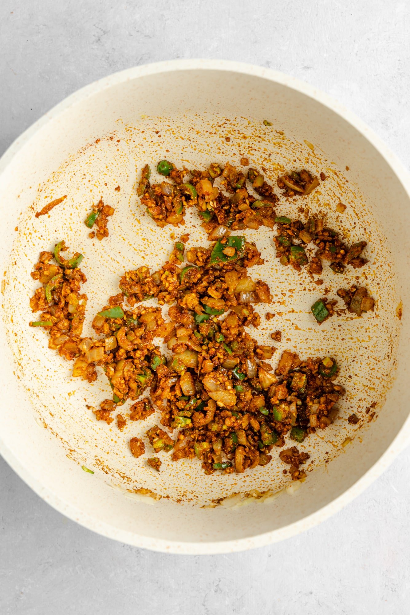 cooked aromatics covered in spices in a large white pot.