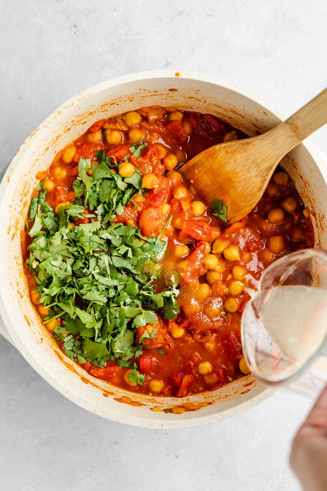 pouring lemon juice into a large pot filled with chana masala.