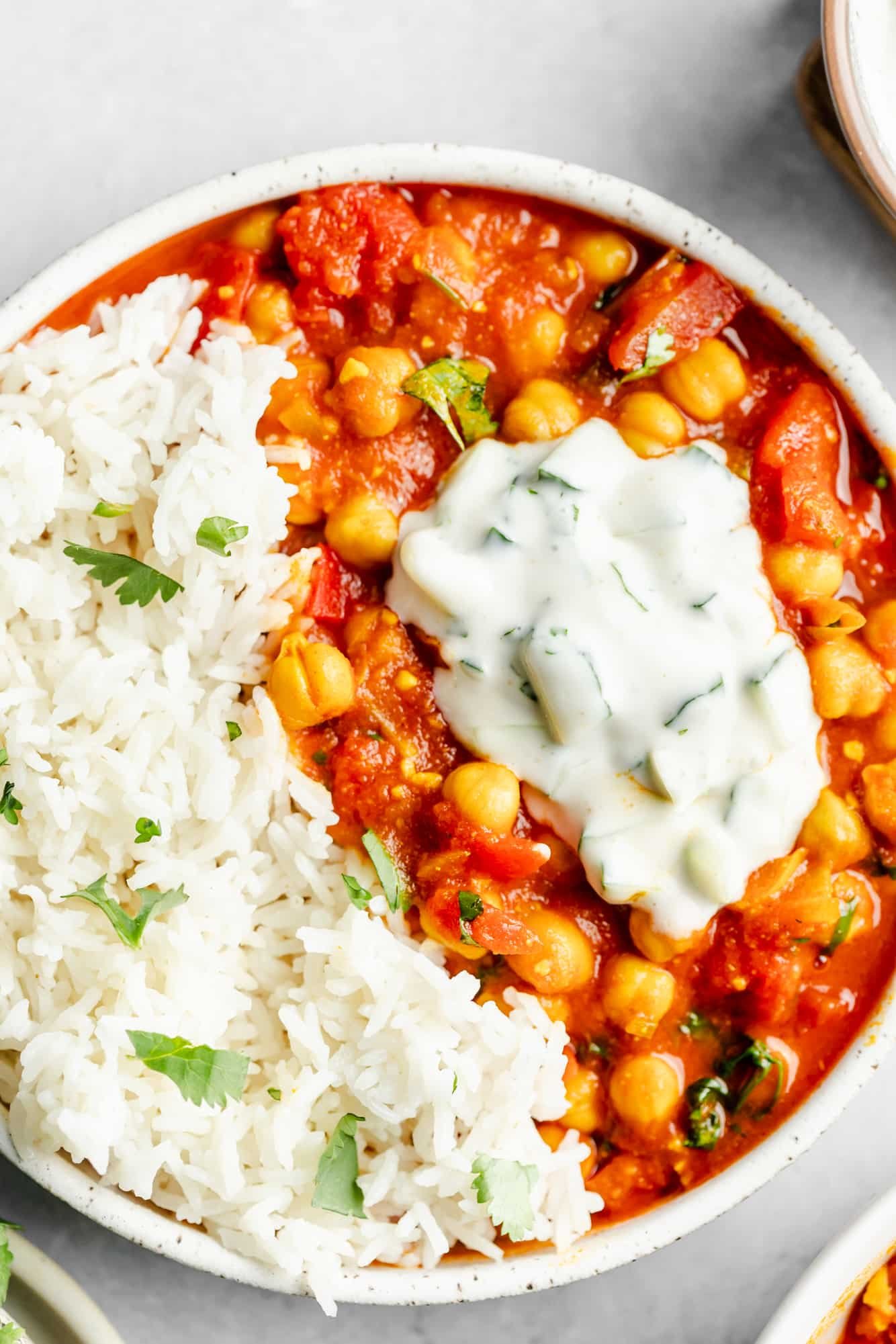 vegan chana masala in a bowl with rice and topped with a dollop of raita.