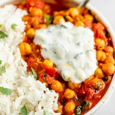 close up on a dollop of raita on top of chana masala in a bowl.