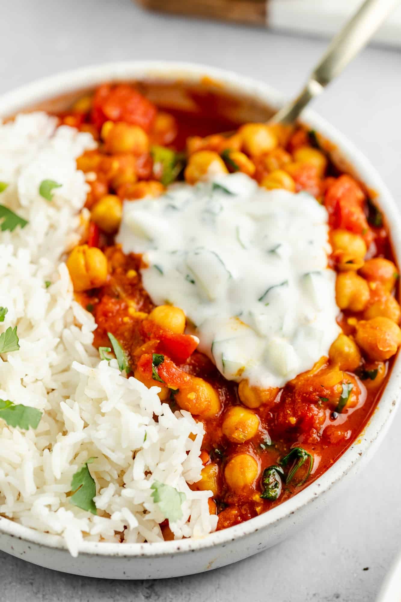 vegan chana masala in a bowl with rice and topped with a dollop of raita.