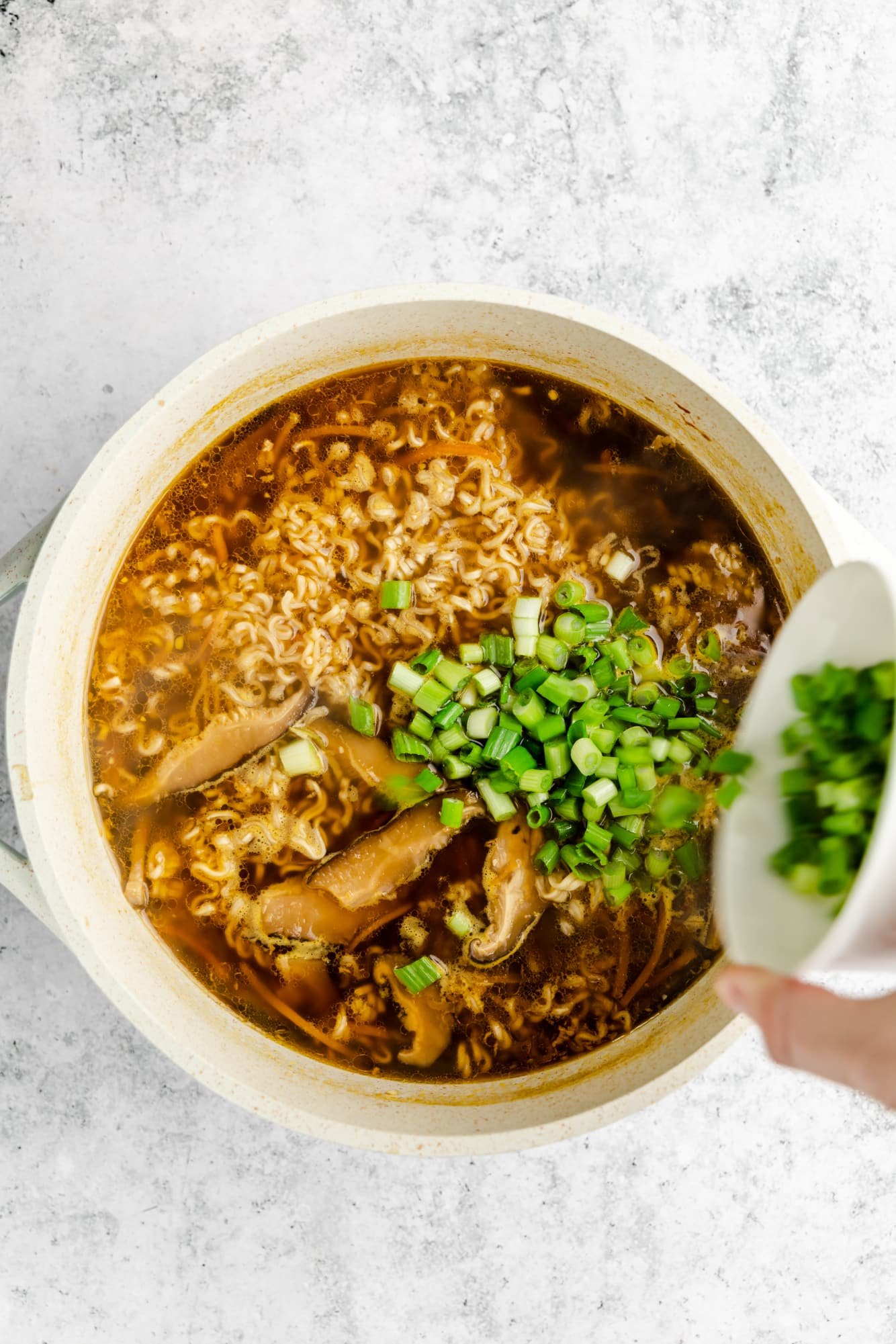 pouring diced scallions into a large pot of vegan ramen.