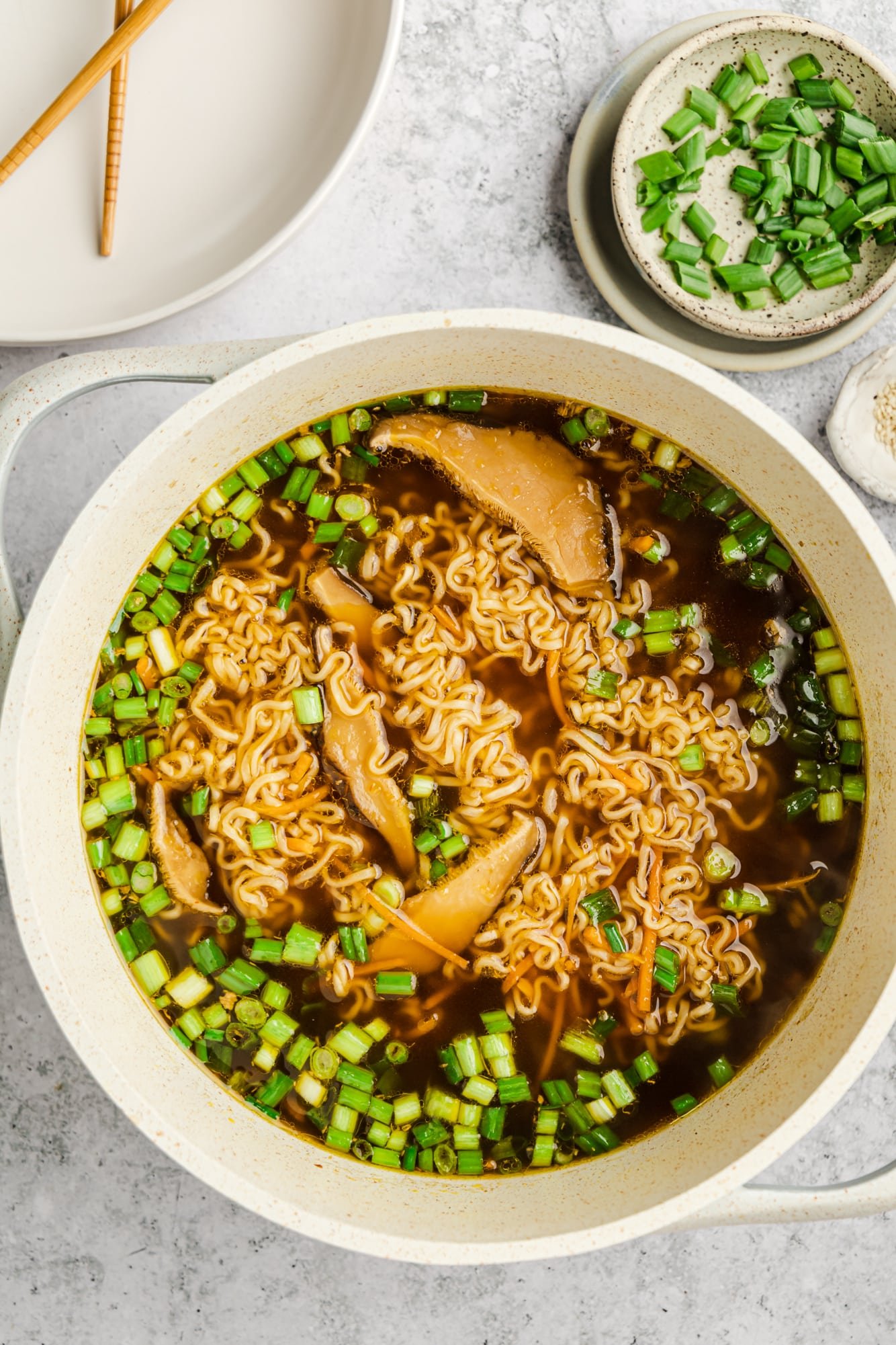 a large pot of vegan ramen next to a small bowl of scallions.