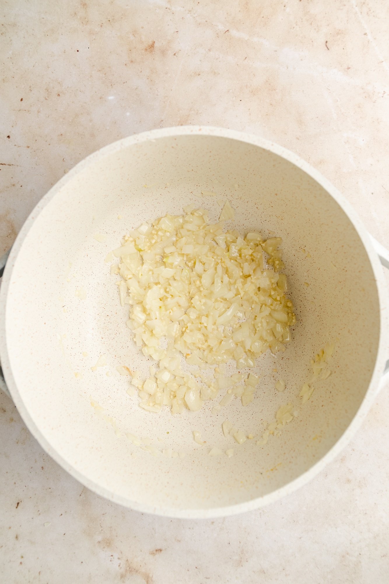 sauteeing onion and garlic in a large white pot.