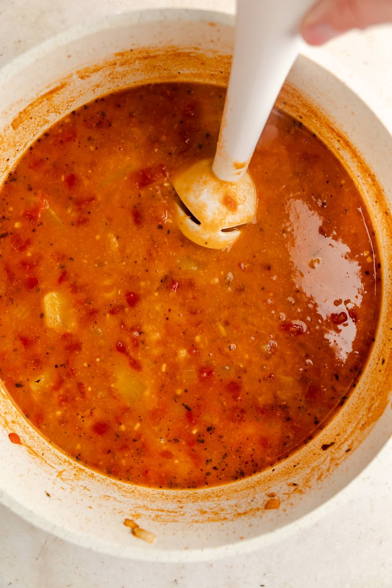 using a white immersion blender to blend chickpea soup in a white pot.