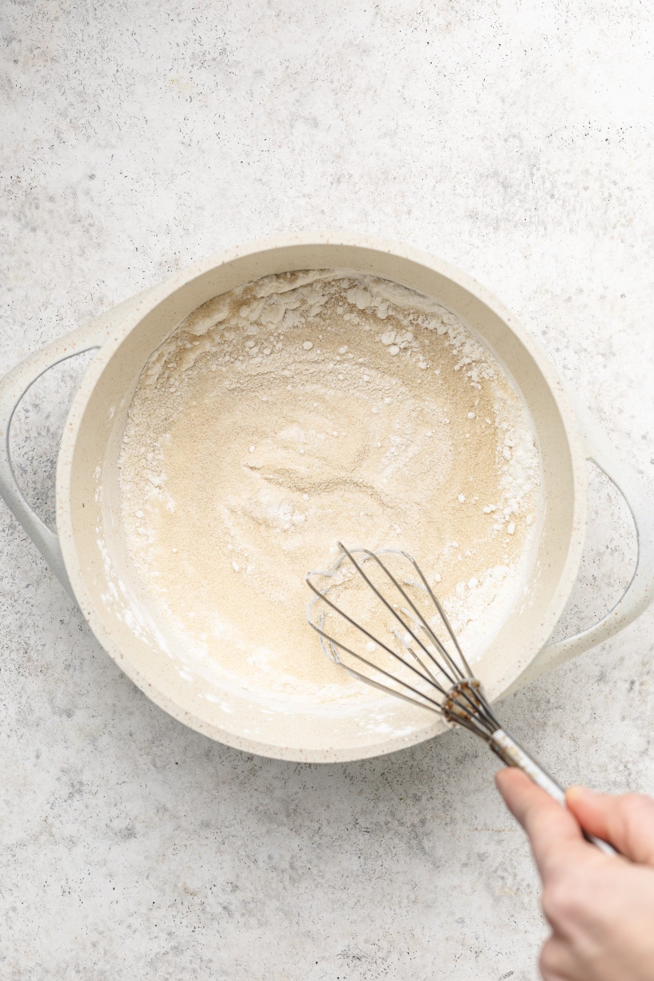 whisking the ingredients for vegan vanilla pudding in a white pot.