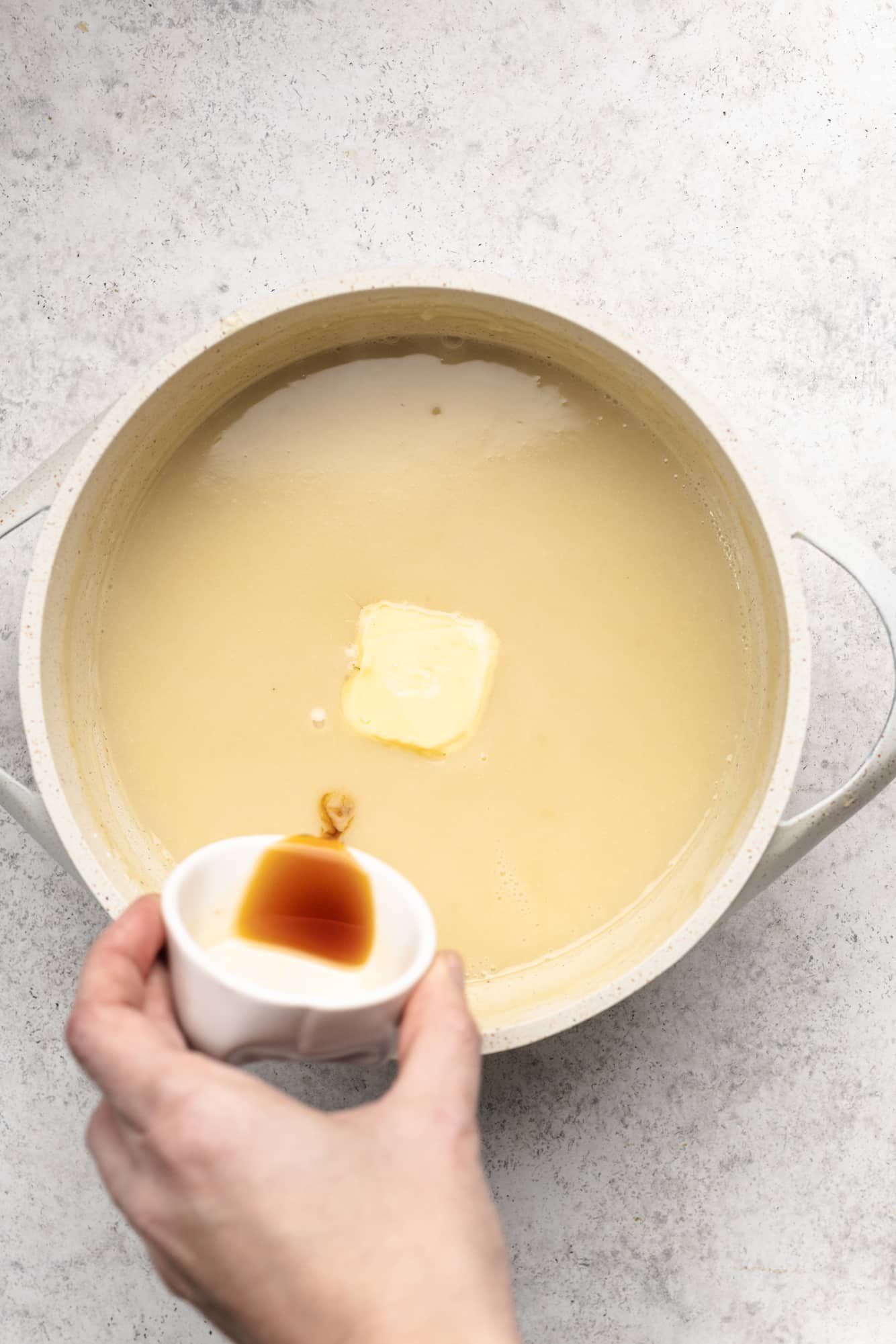 womans hand pouring butter and vanilla extract into a pot full of vegan vanilla pudding.