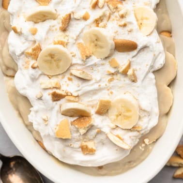close up on an assembled vegan banana pudding topped with whipped cream, crushed cookies, and banana slices.