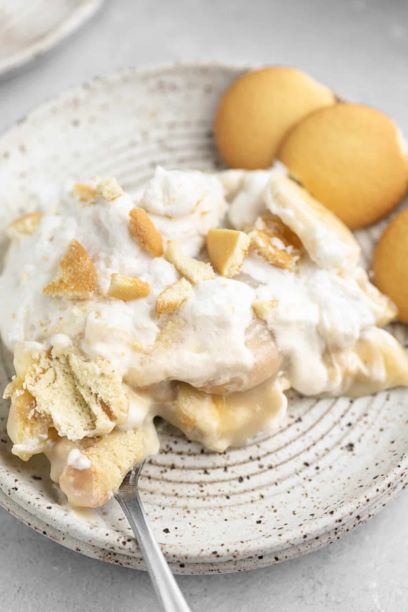 a scoop of vegan banana pudding on a small white plate with vanilla wafer cookies on the side.