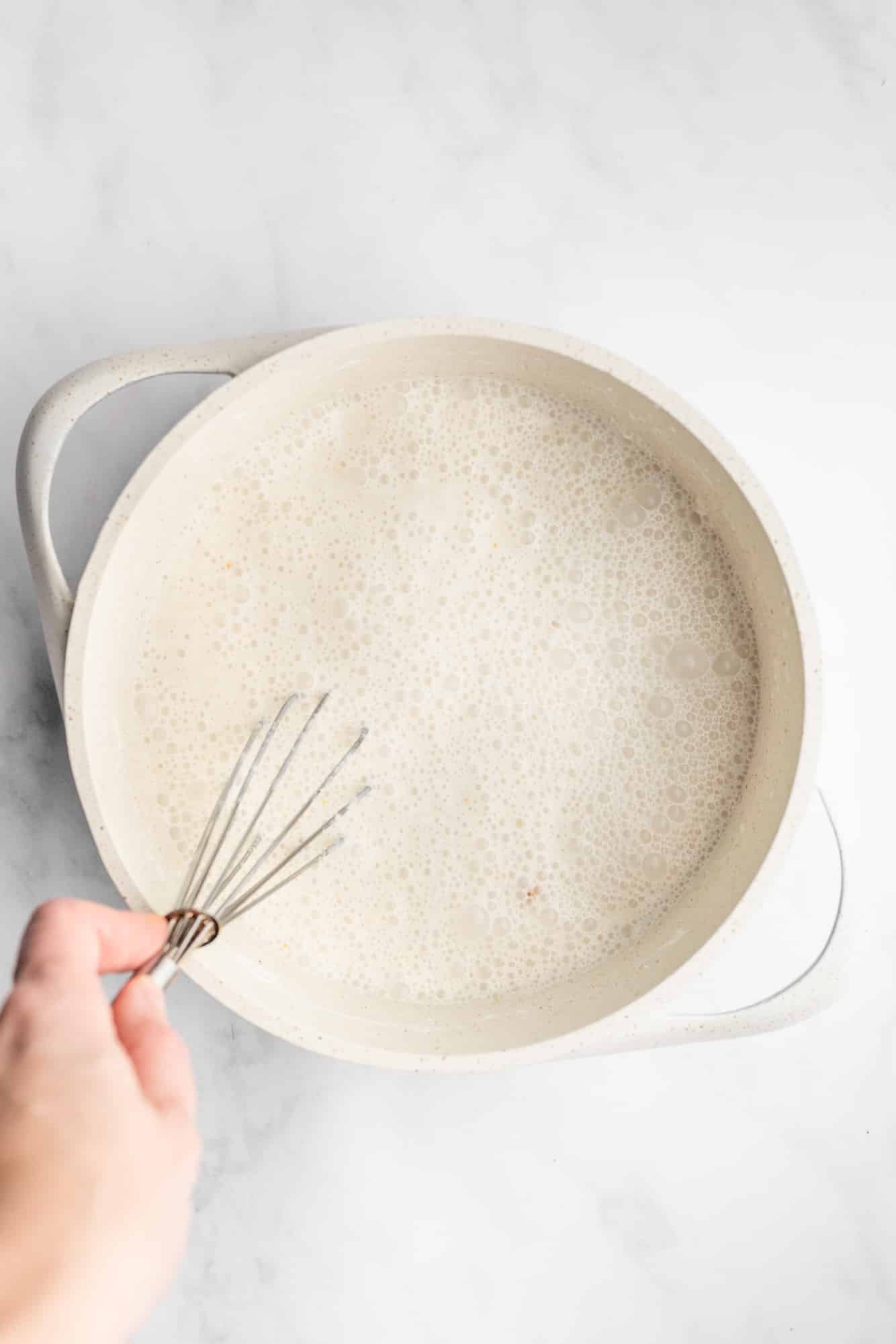 womans hand whisking a creamy white custard in a large white dish.