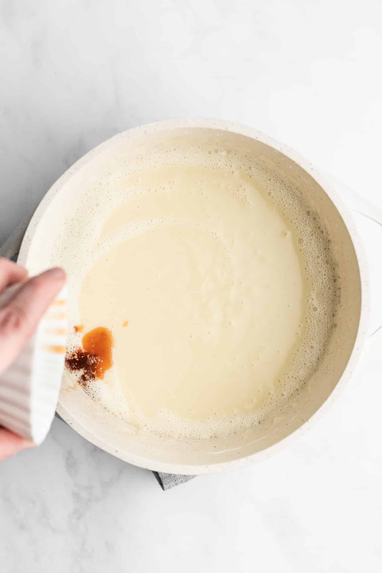 womans hand pouring vanilla extract into a creamy white custard.