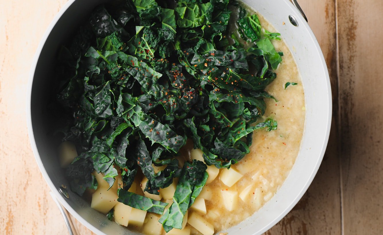 Kale, potatoes and broth in a large gray bowl.