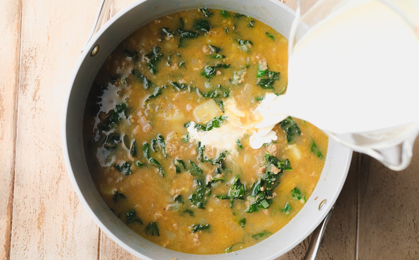 pouring cream into a pot of zuppa toscana soup.