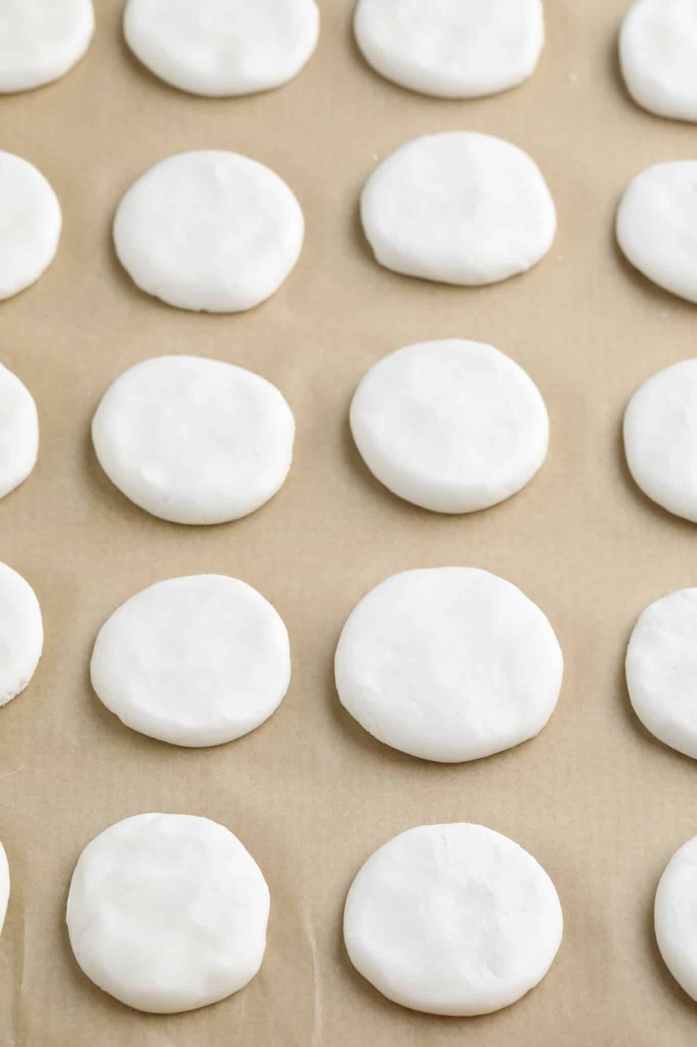 white discs in rows on a parchment-lined baking sheet.