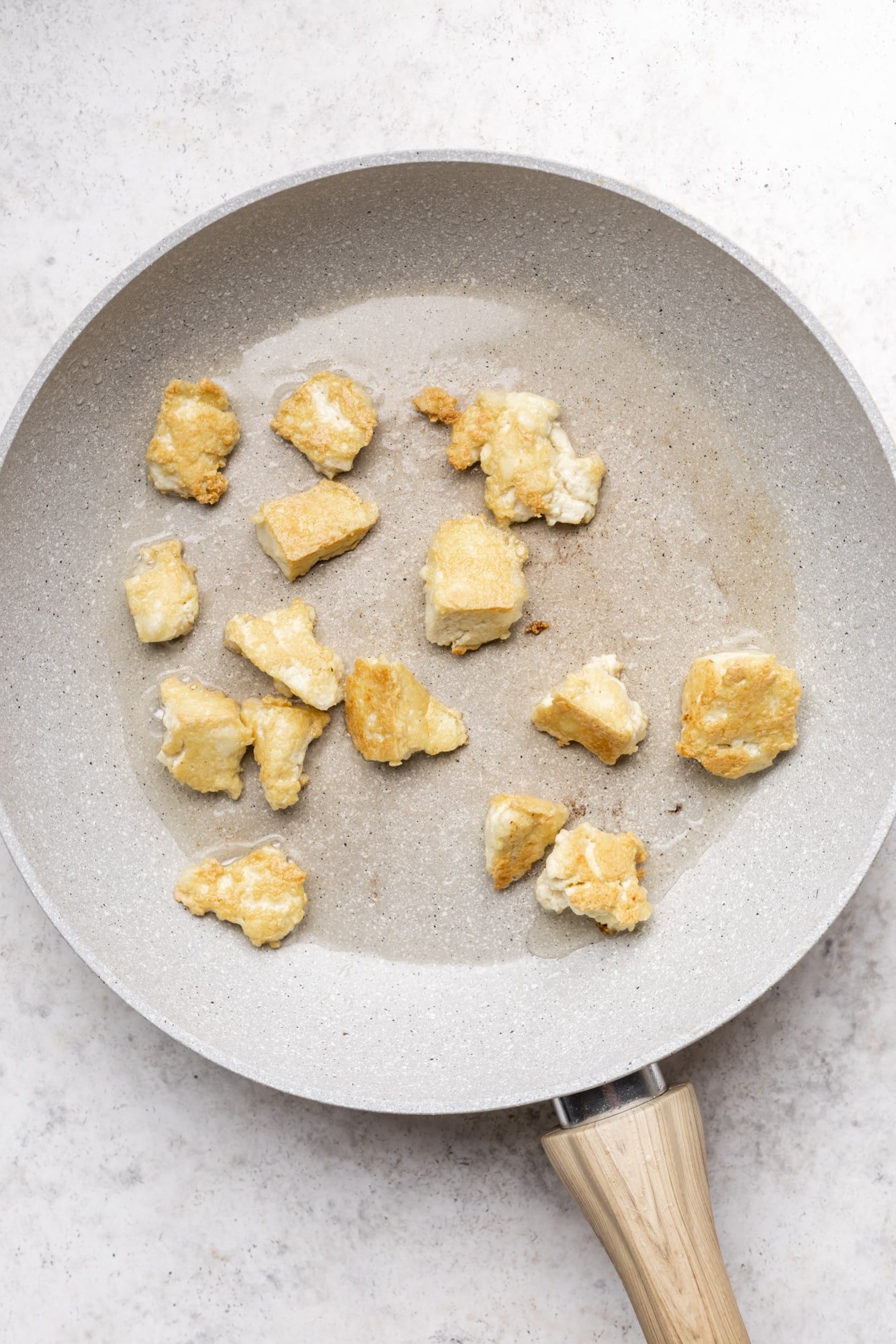 frying tofu chunks in an oiled grey pan.