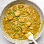 stirring yellow tofu curry in a grey pan with a white spatula.