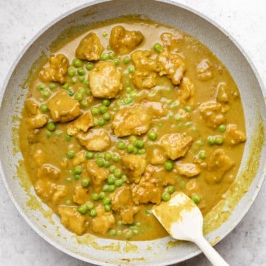 stirring yellow tofu curry in a grey pan with a white spatula.