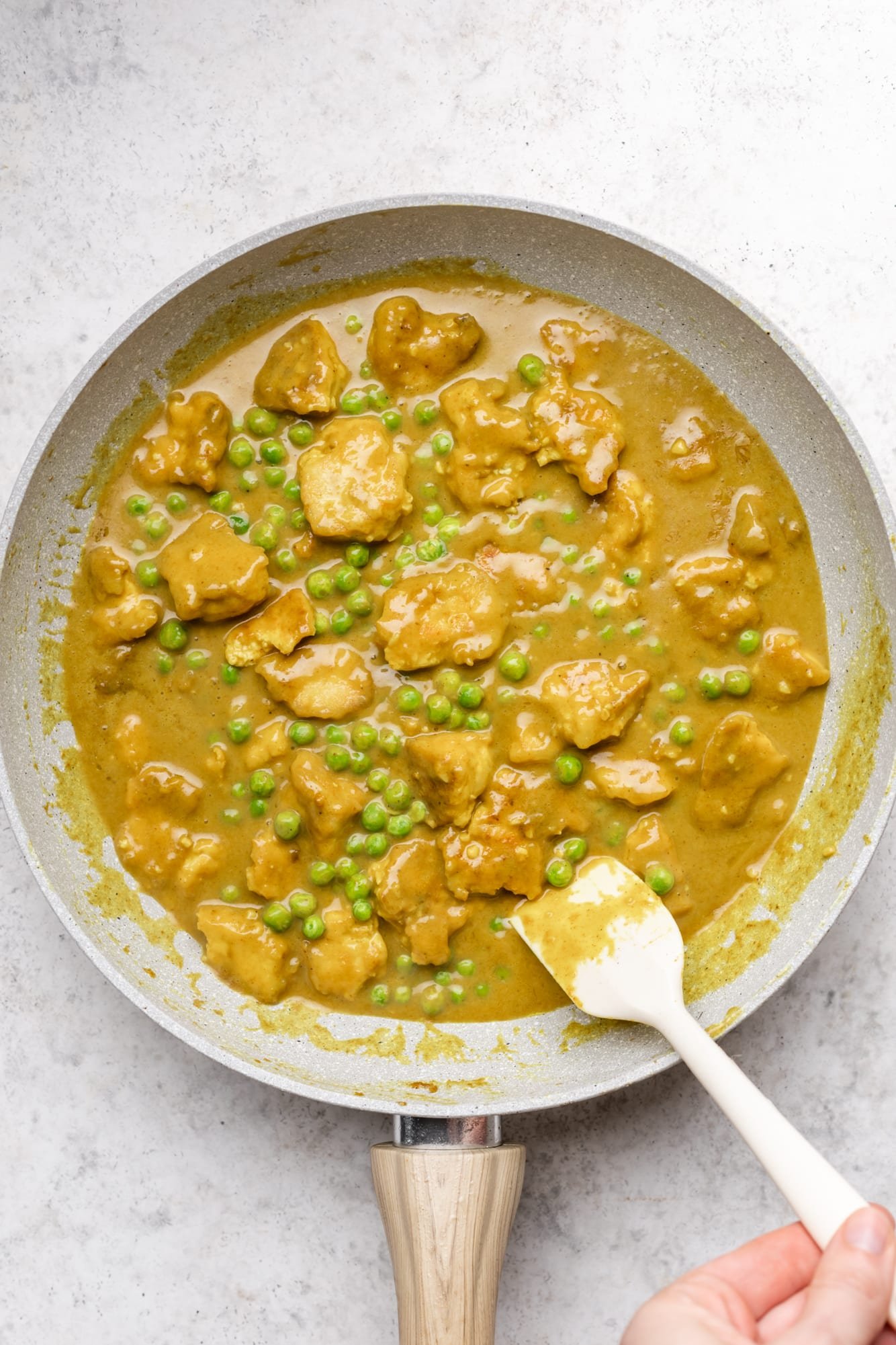 stirring yellow tofu curry in a grey pan with a white spatula.