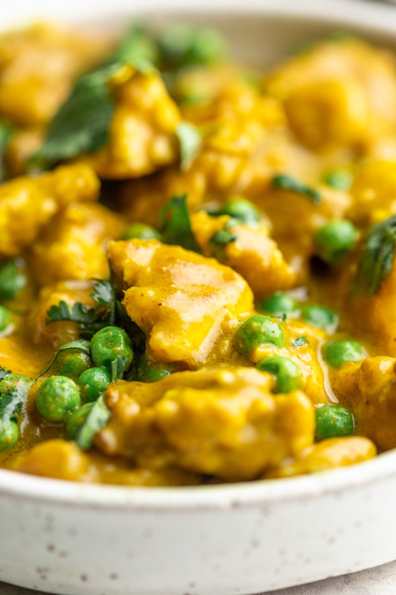 close up on a bowl of tofu curry with green peas and cilantro.