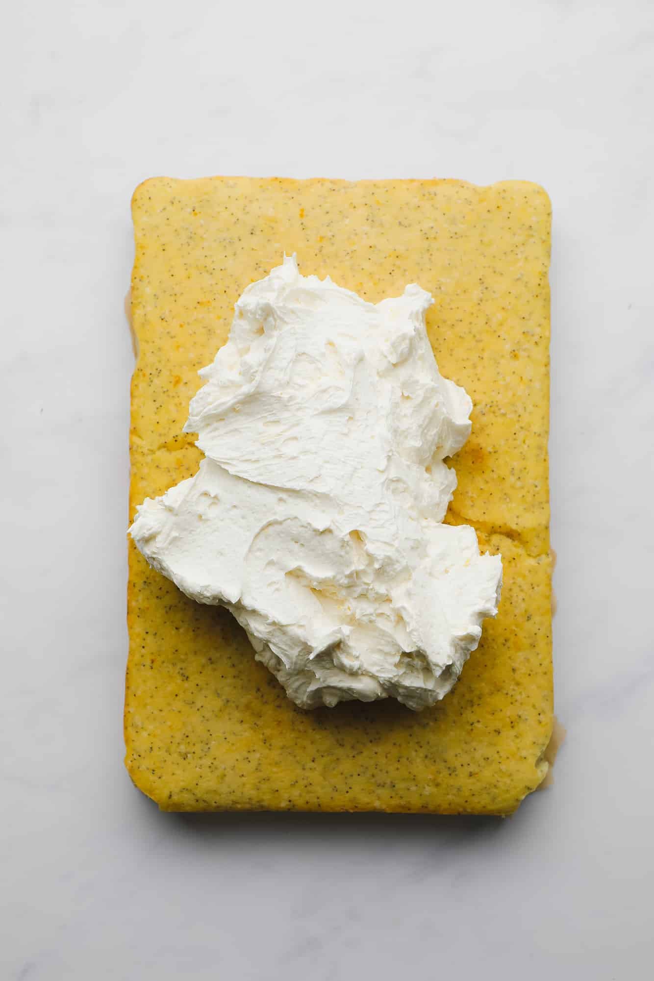 a pile of white buttercream on top of a baked rectangular lemon poppyseed cake.