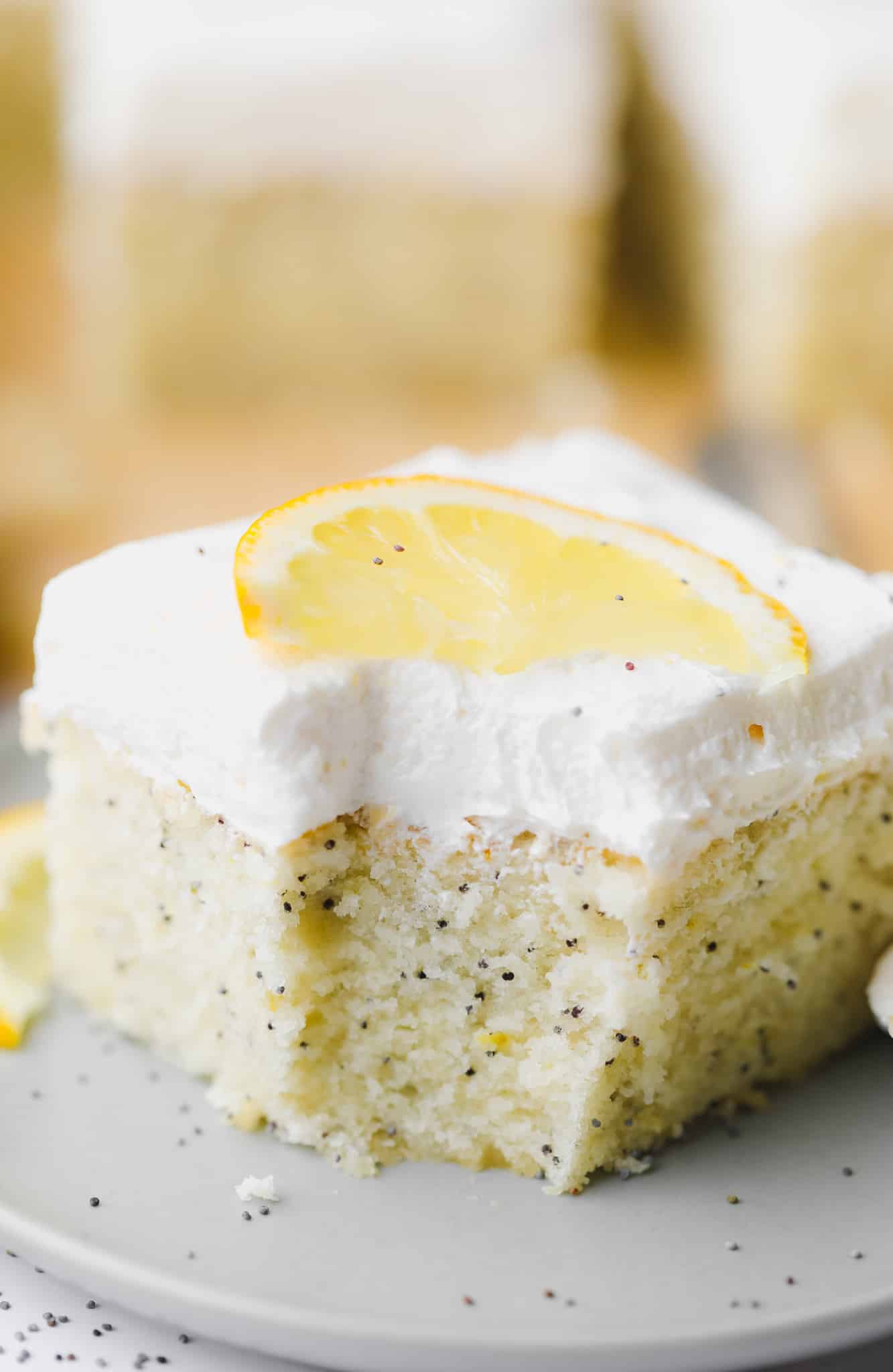 a piece of vegan lemon poppyseed cake with a bite removed on a small grey plate.