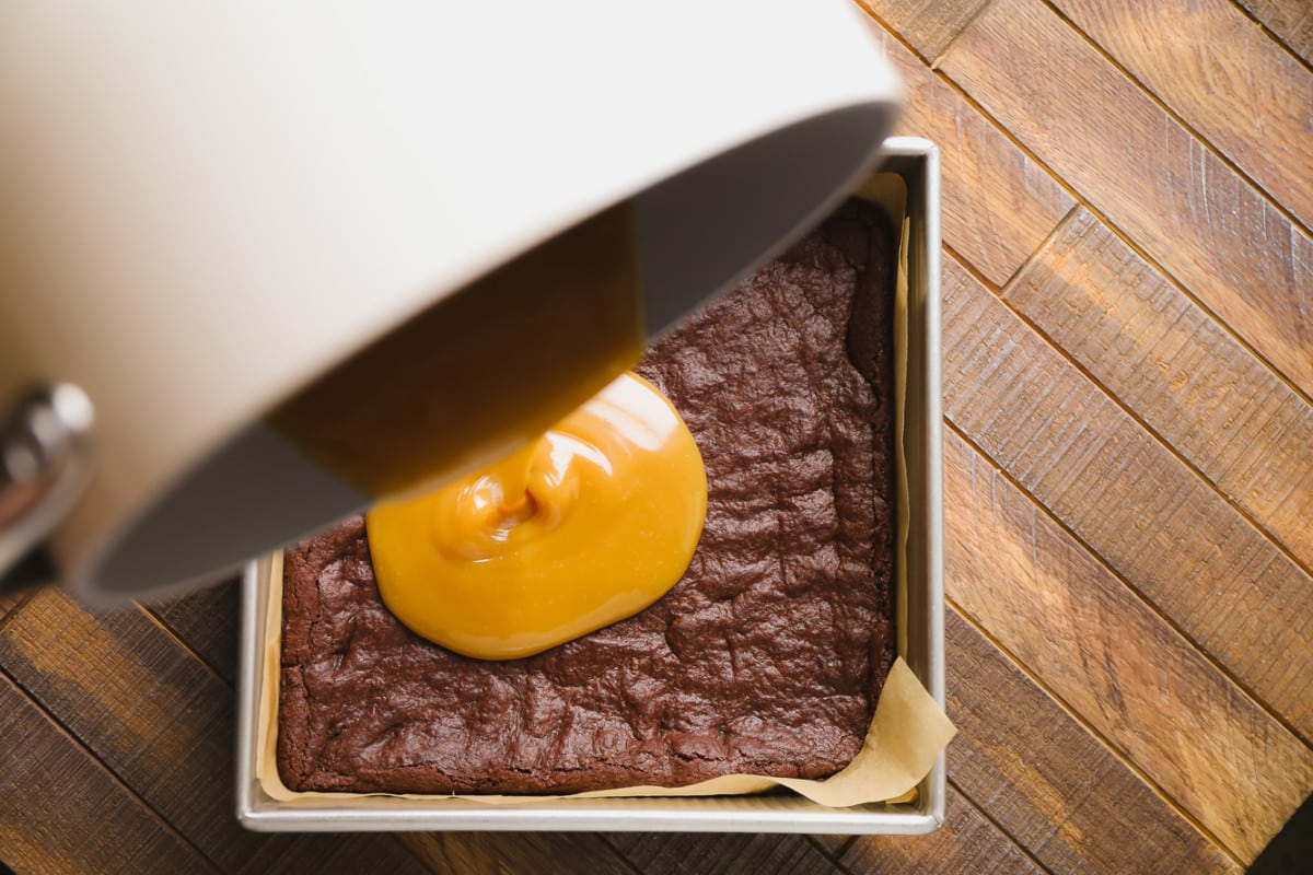 caramel being poured over brownies in a pan.