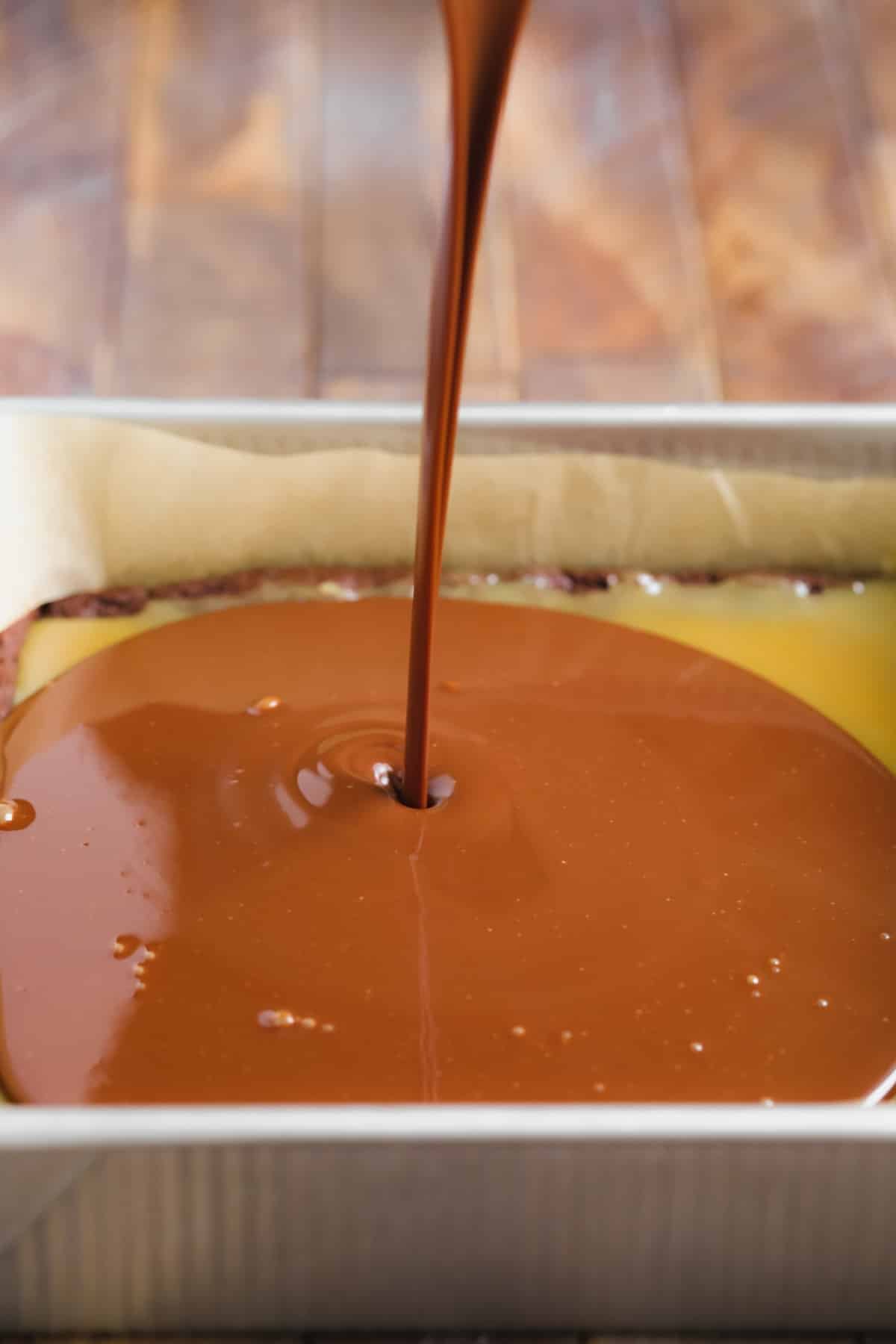 chocolate being poured on top of a caramel layer in a pan.
