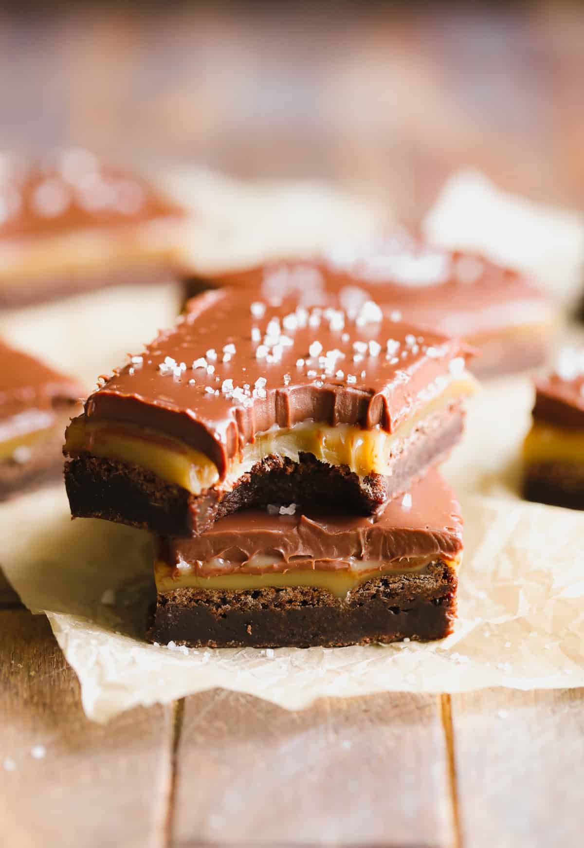 two brownies with caramel middle and chocolate topping and salt, on parchment paper.