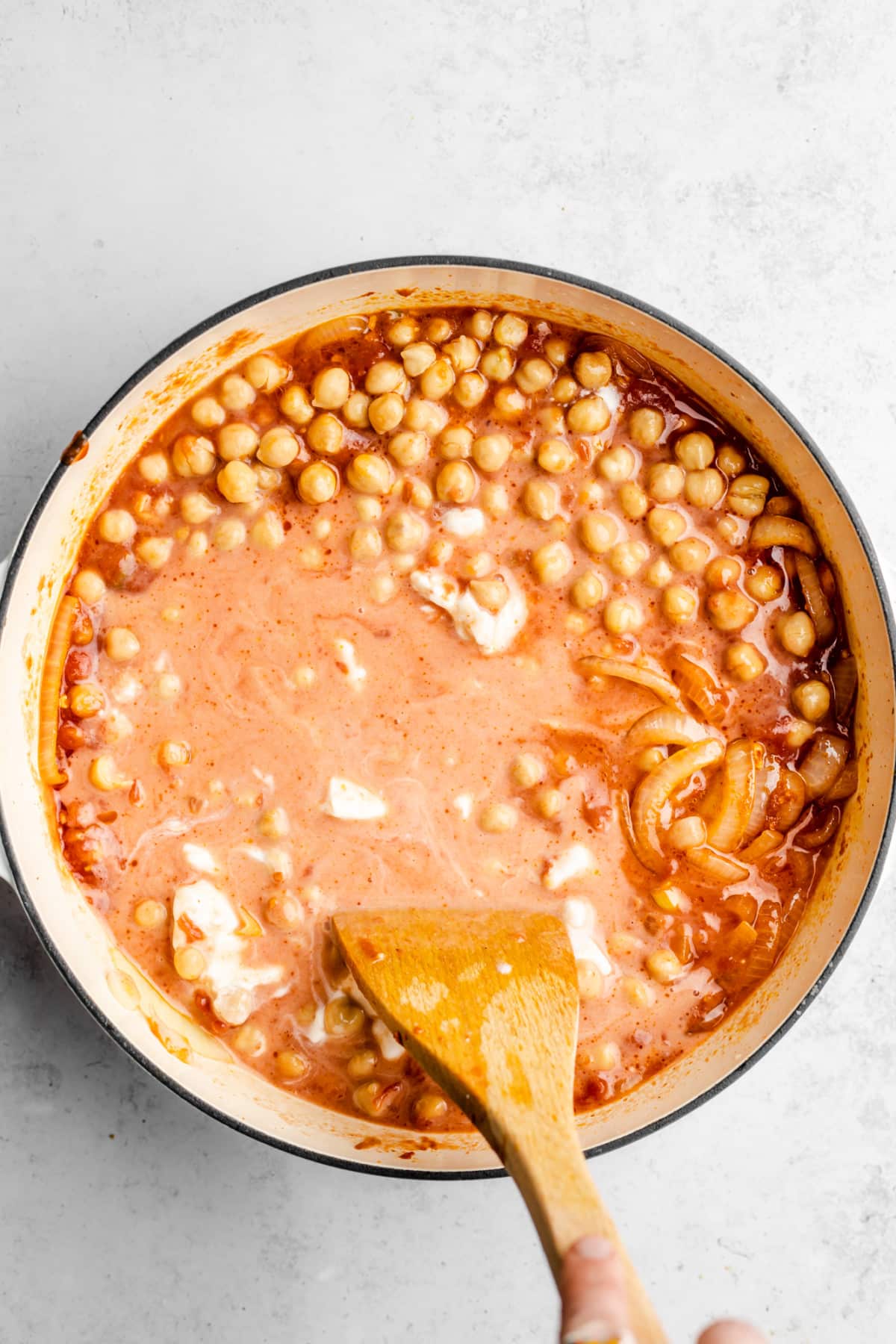 white cream being added to a pot with chickpeas and onions in a reddish sauce