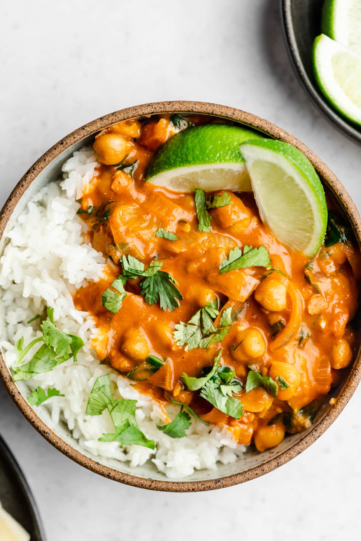 looking down on a bowl of rice and reddish creamy sauce with chickpeas and a few lime wedges.