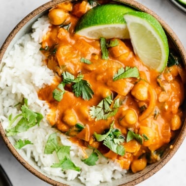 close up of a bowl with creamy tomato chickpeas, white rice and limes