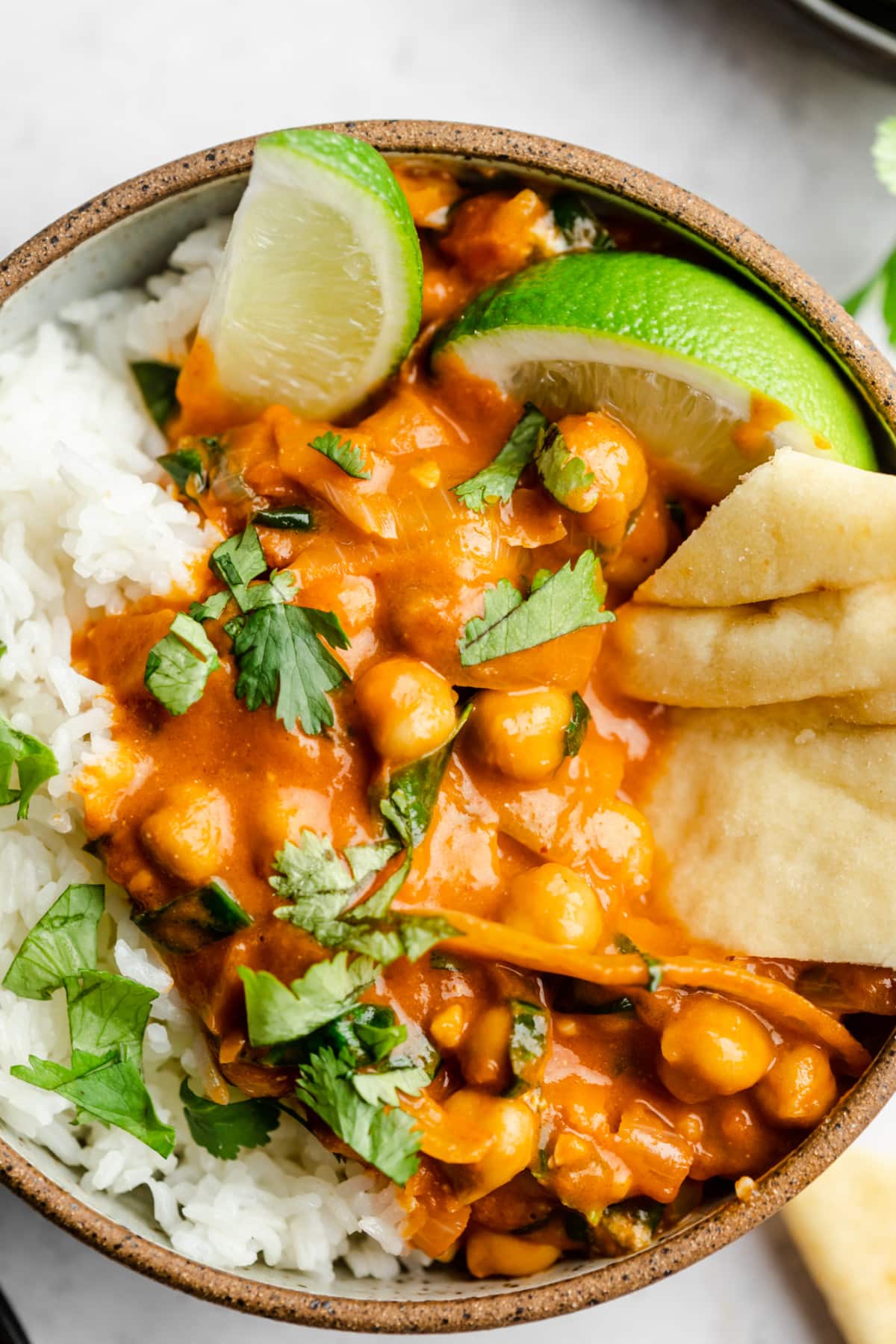 brown rimmed bowl on white background with creamy chickpeas, rice, naan and chopped cilantro