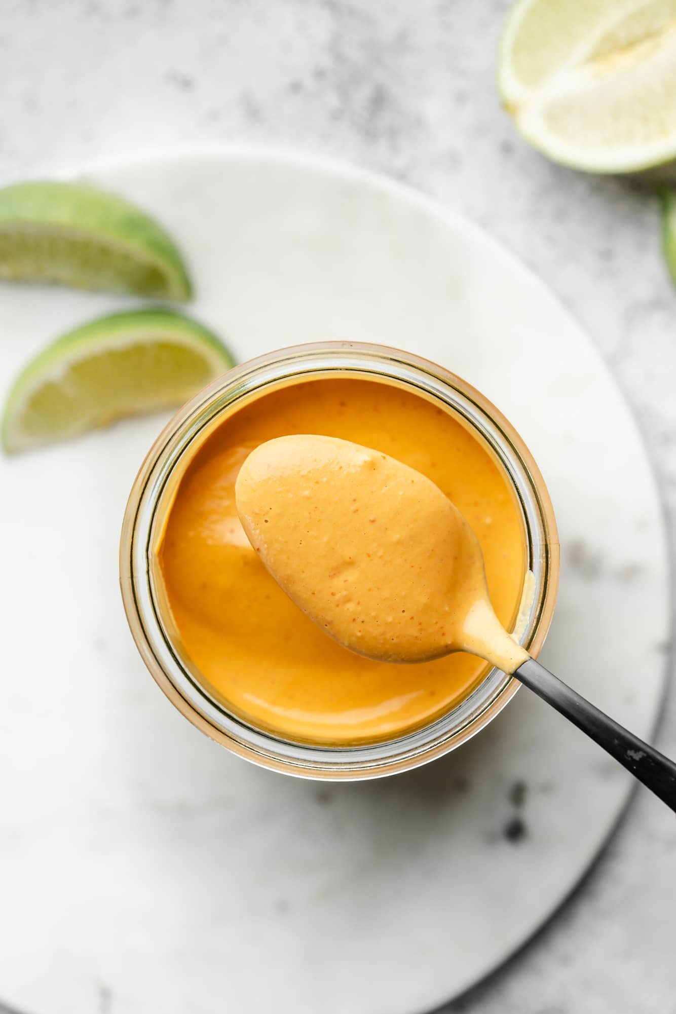 a spoon lifting up a scoop of chipotle sauce from a jar of the sauce.