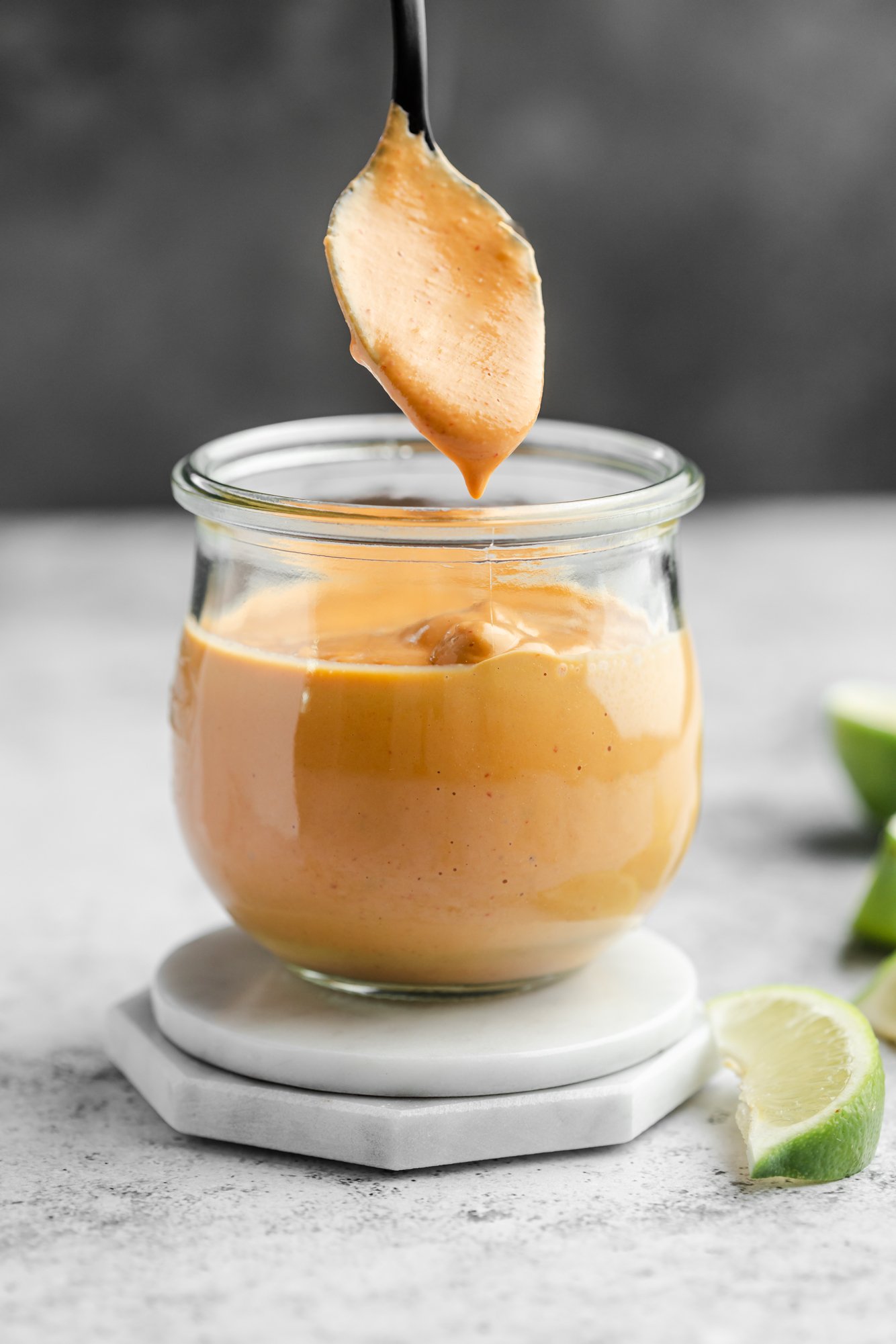 a spoon lifting up from a small glass jar of orange chipotle sauce.