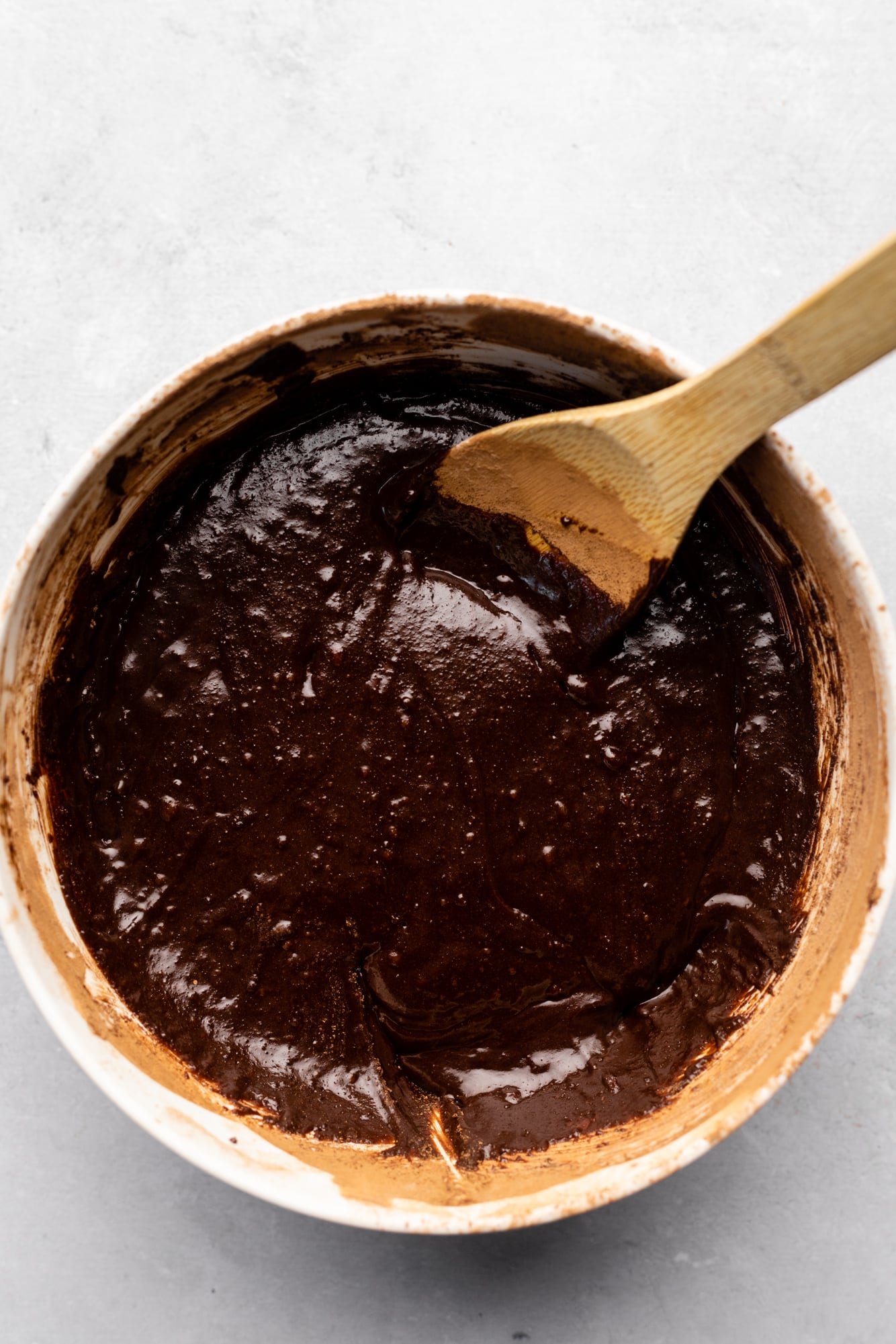 using a wood spoon to stir brownie batter in a large white bowl.