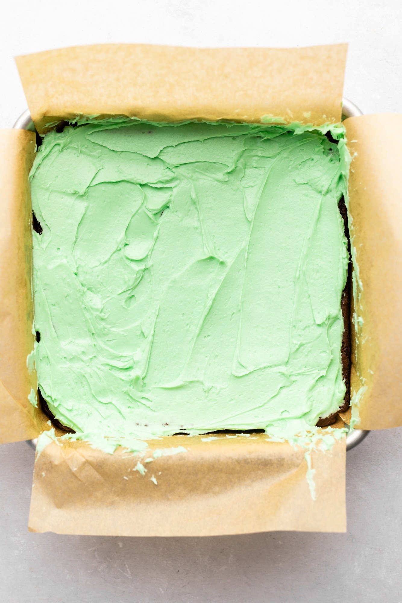 mint green frosting on top of baked brownies in a pan.