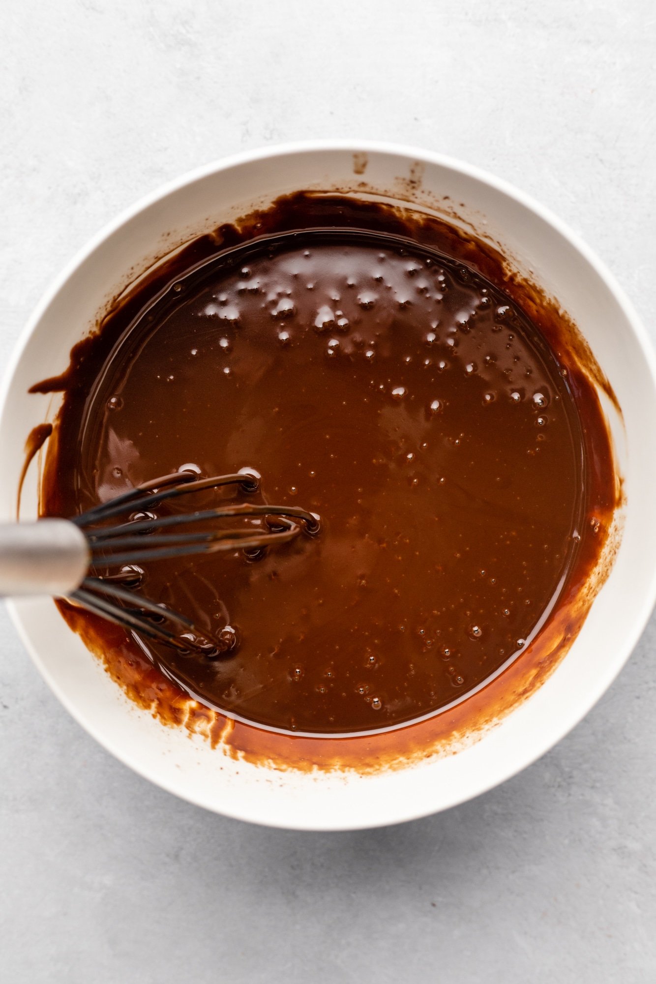 using a whisk to stir chocolate ganache in a large white bowl.