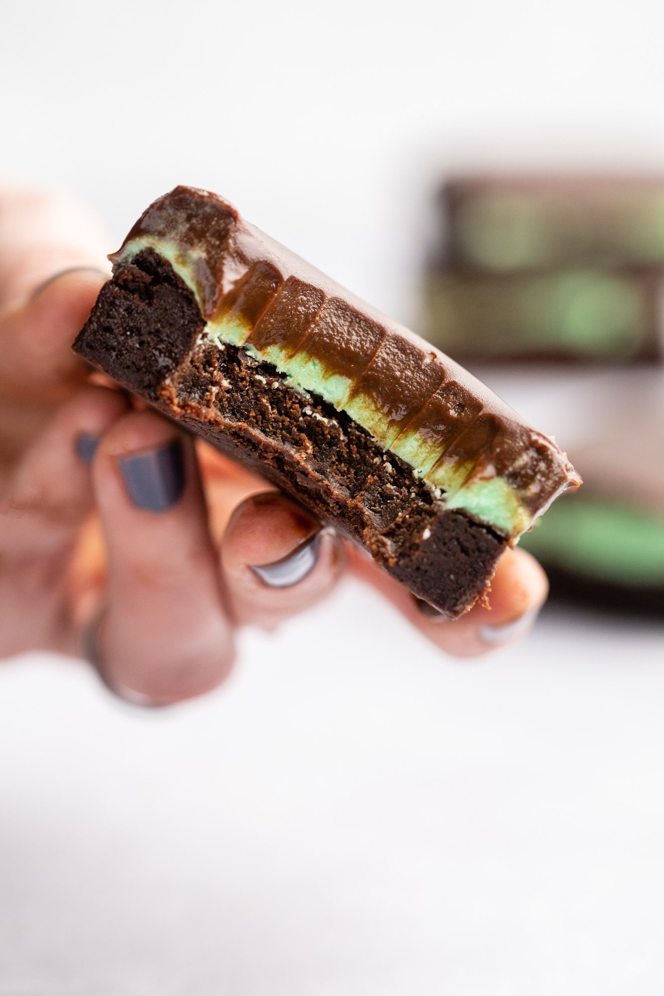 womans hand holding a chocolate mint brownie with a bite taken out of it.