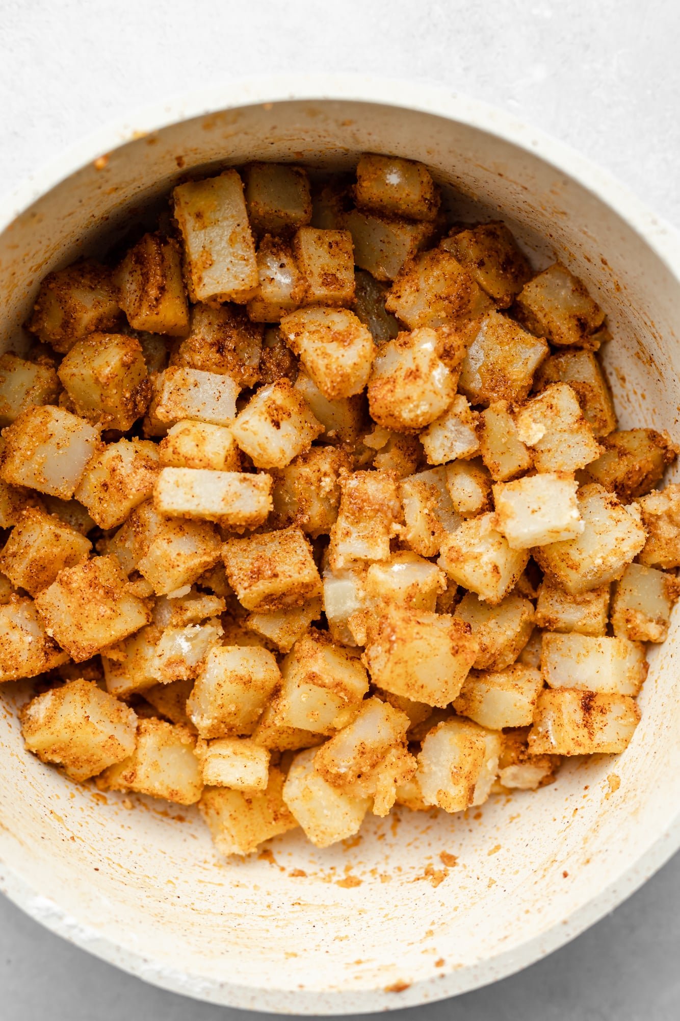Slice boiled and seasoned potatoes in a large white bowl.