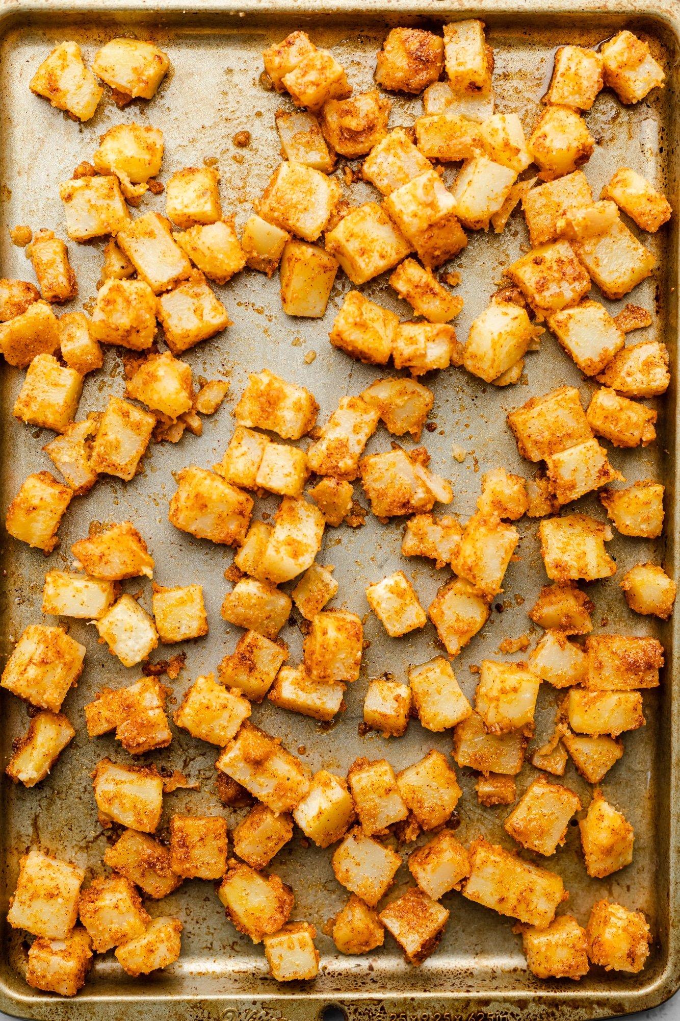 Ripe potato chunks are laid out on a large baking sheet.