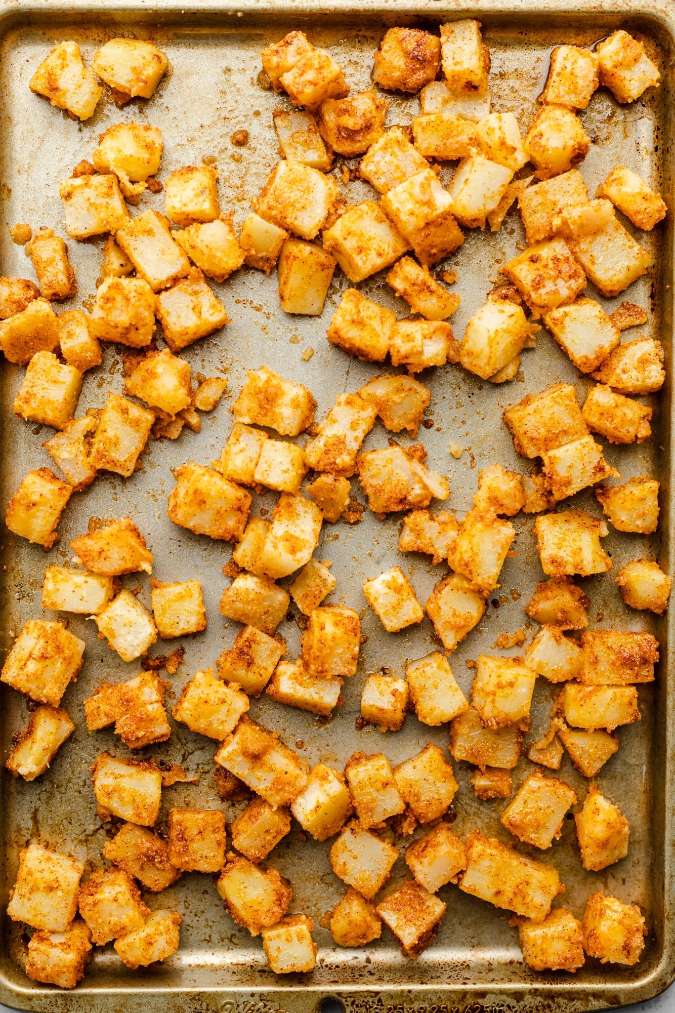 seasoned potato chunks laid out on a large baking sheet.