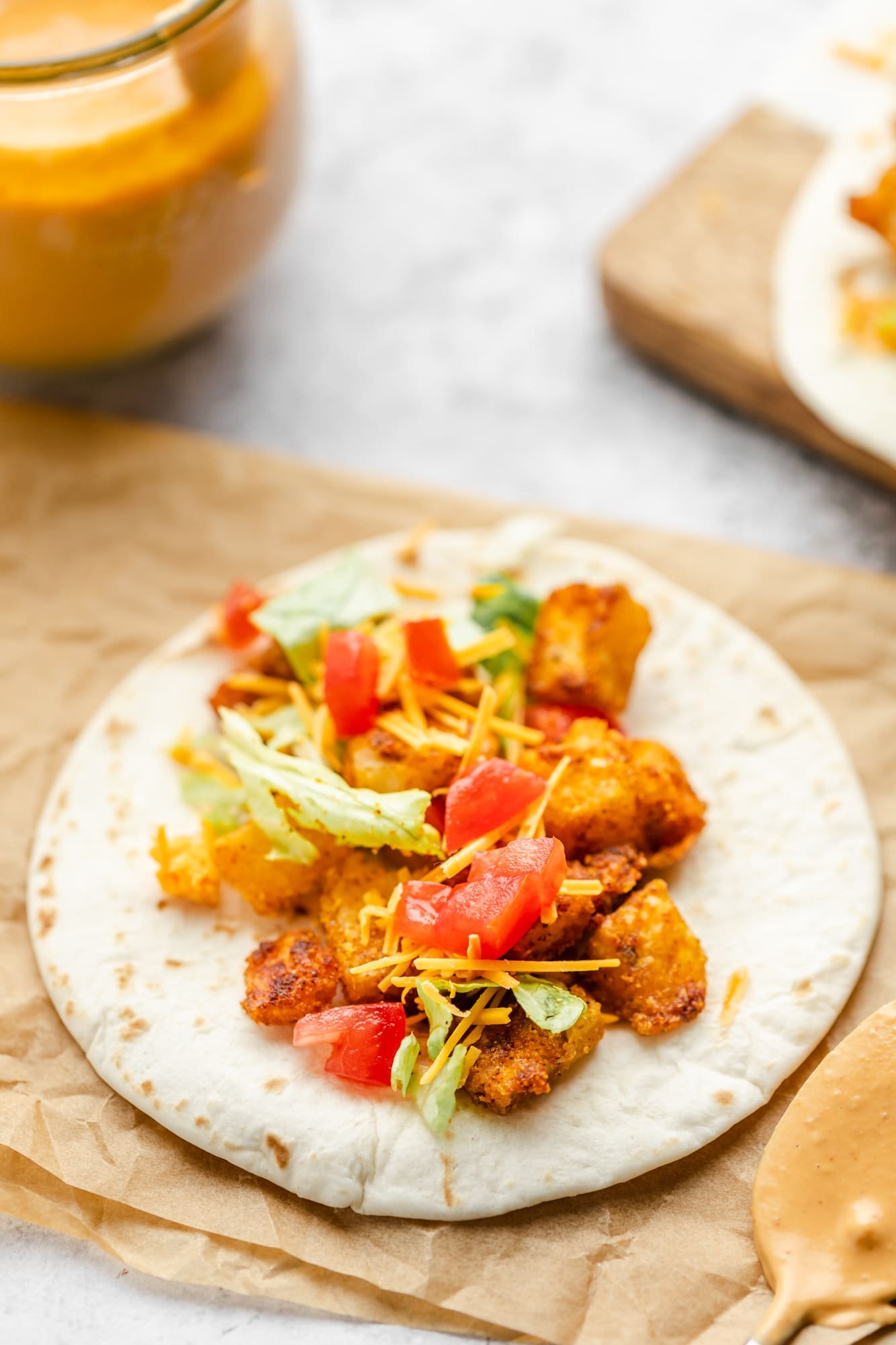 crispy potatoes, tomatoes, lettuce, and cheese on a small flour tortilla.