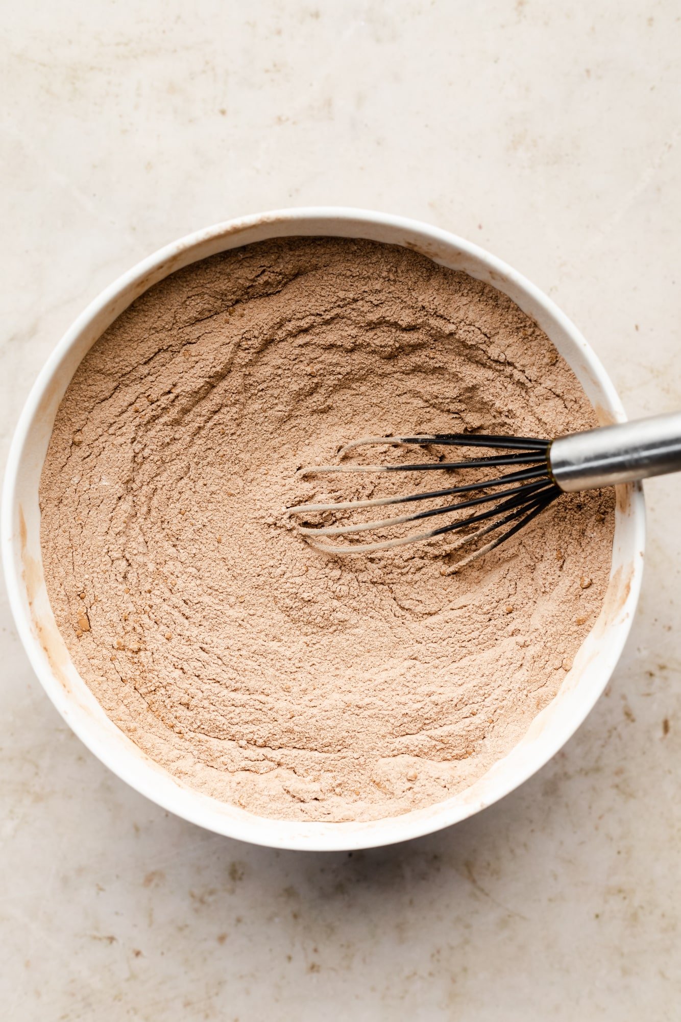 Dry chocolate cake mix in a large white bowl and a whisk.