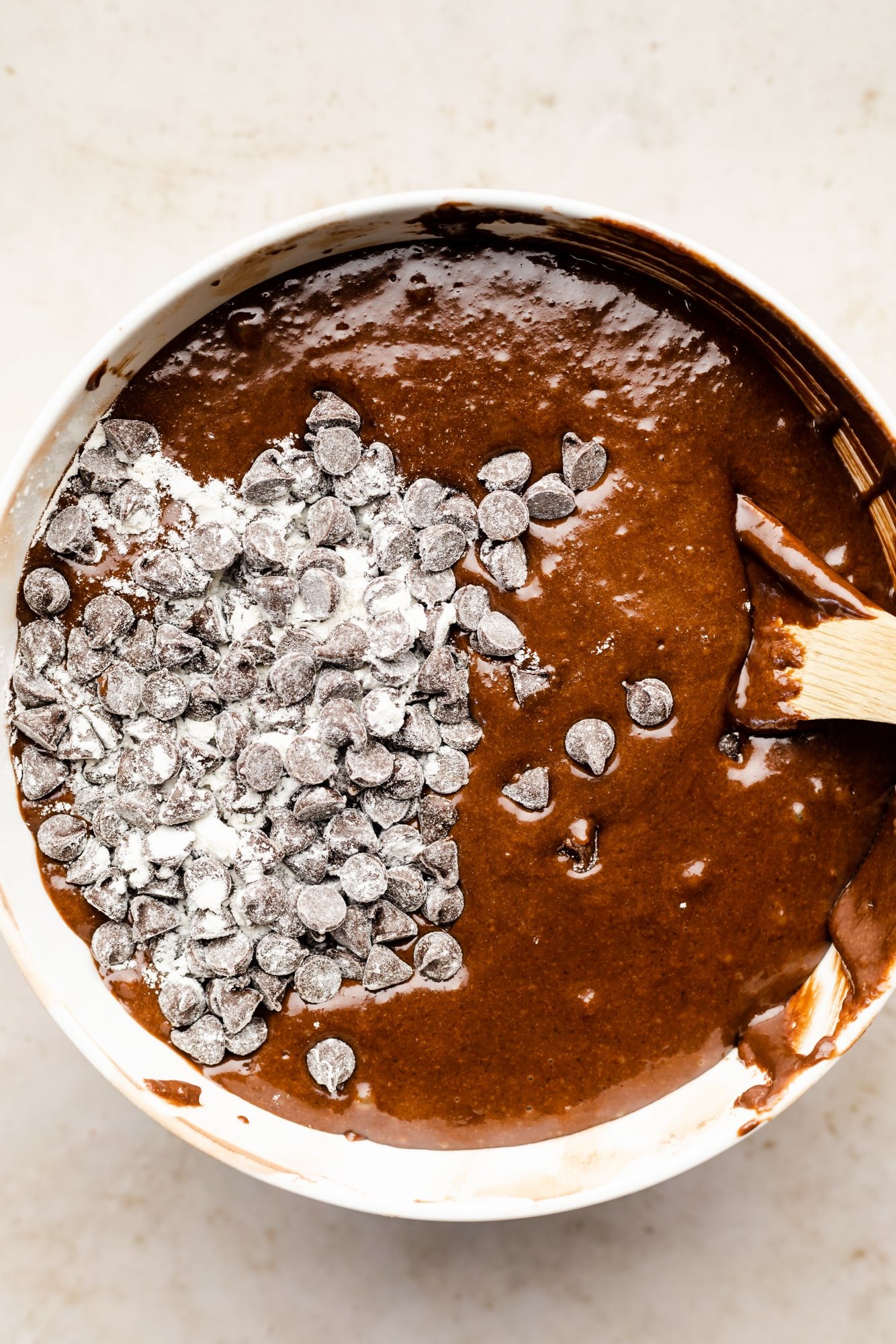 using a wooden spoon to fold chocolate chips into chocolate cake batter.