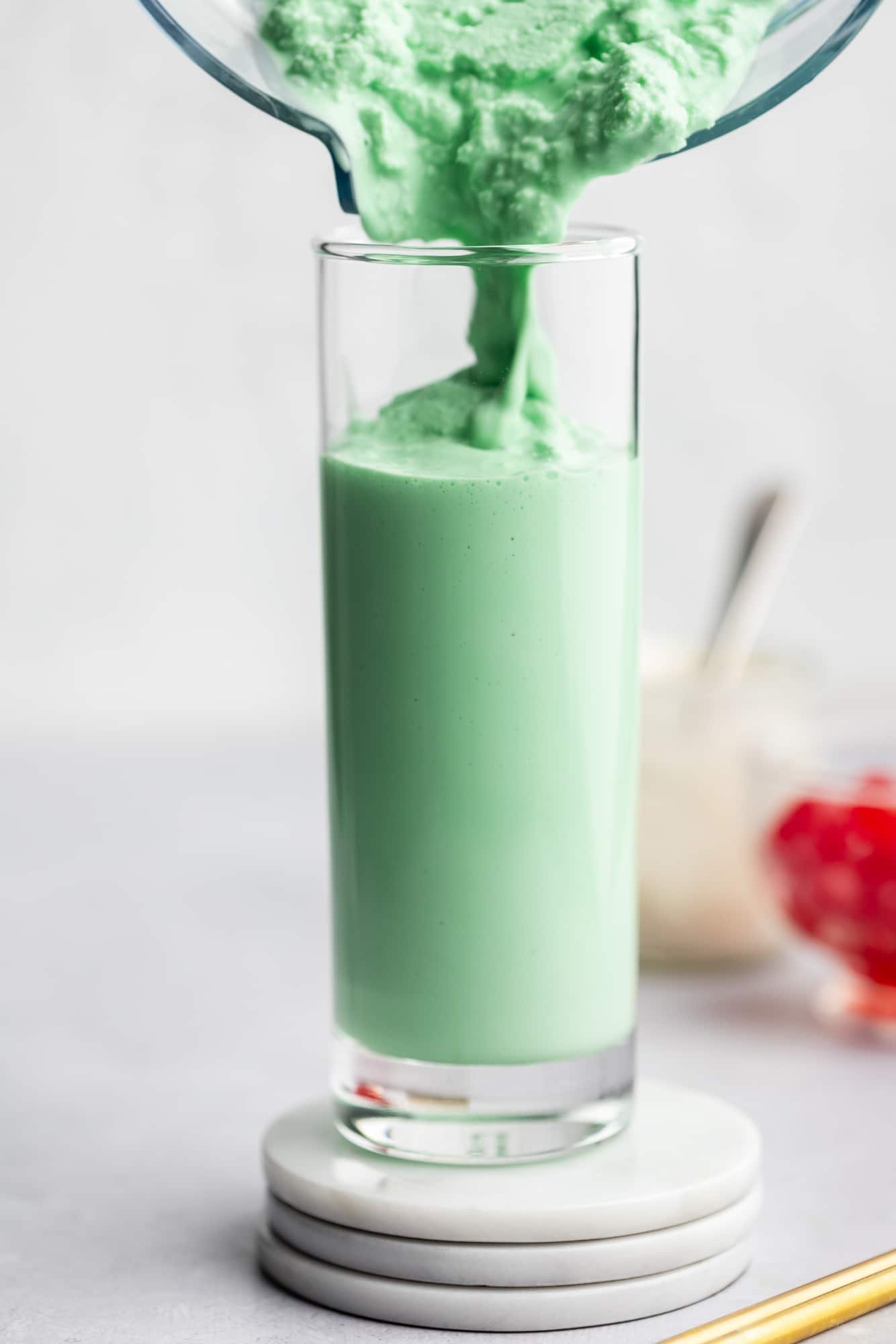 pouring a mint green vegan shamrock shake into a tall glass.