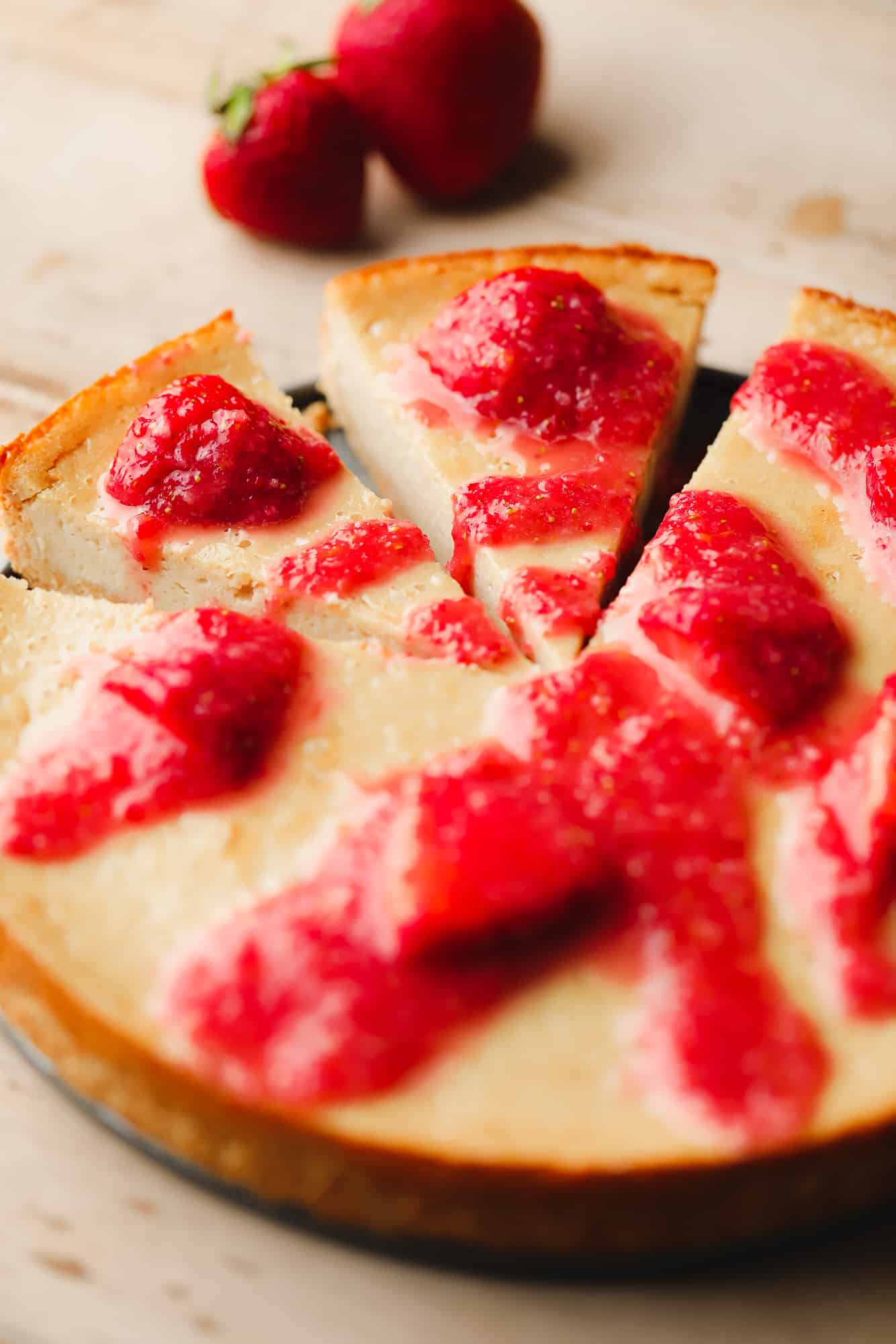 a sliced vegan cashew cheesecake topped with red strawberry sauce.