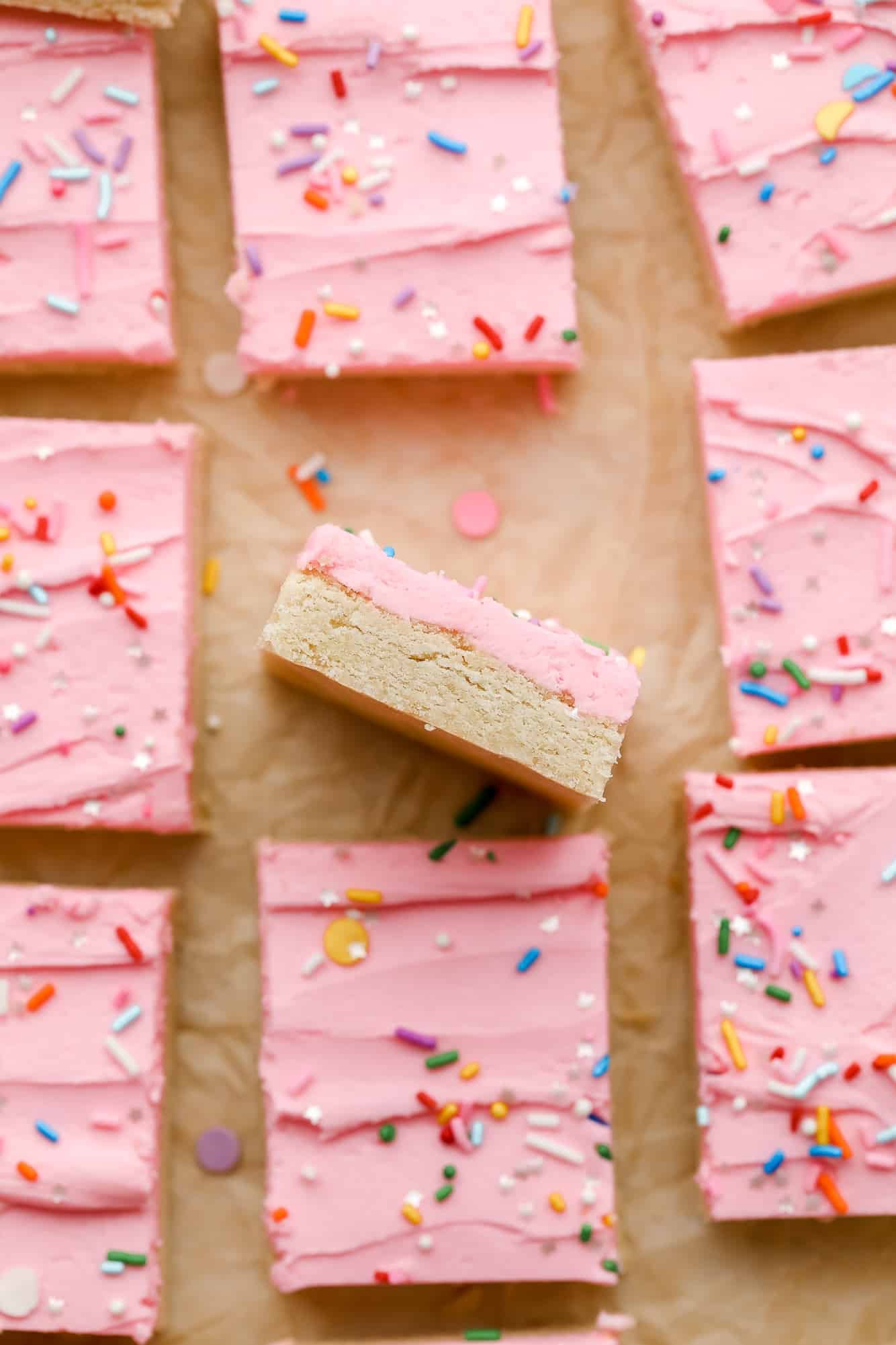 a vegan sugar cookie bar turned on its side next to rows of more bars with pink frosting on top.