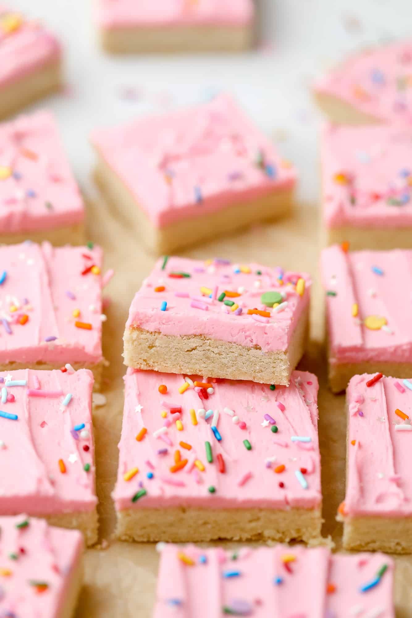 rows of sugar cookie bars decorated with pink frosting and rainbow sprinkles.