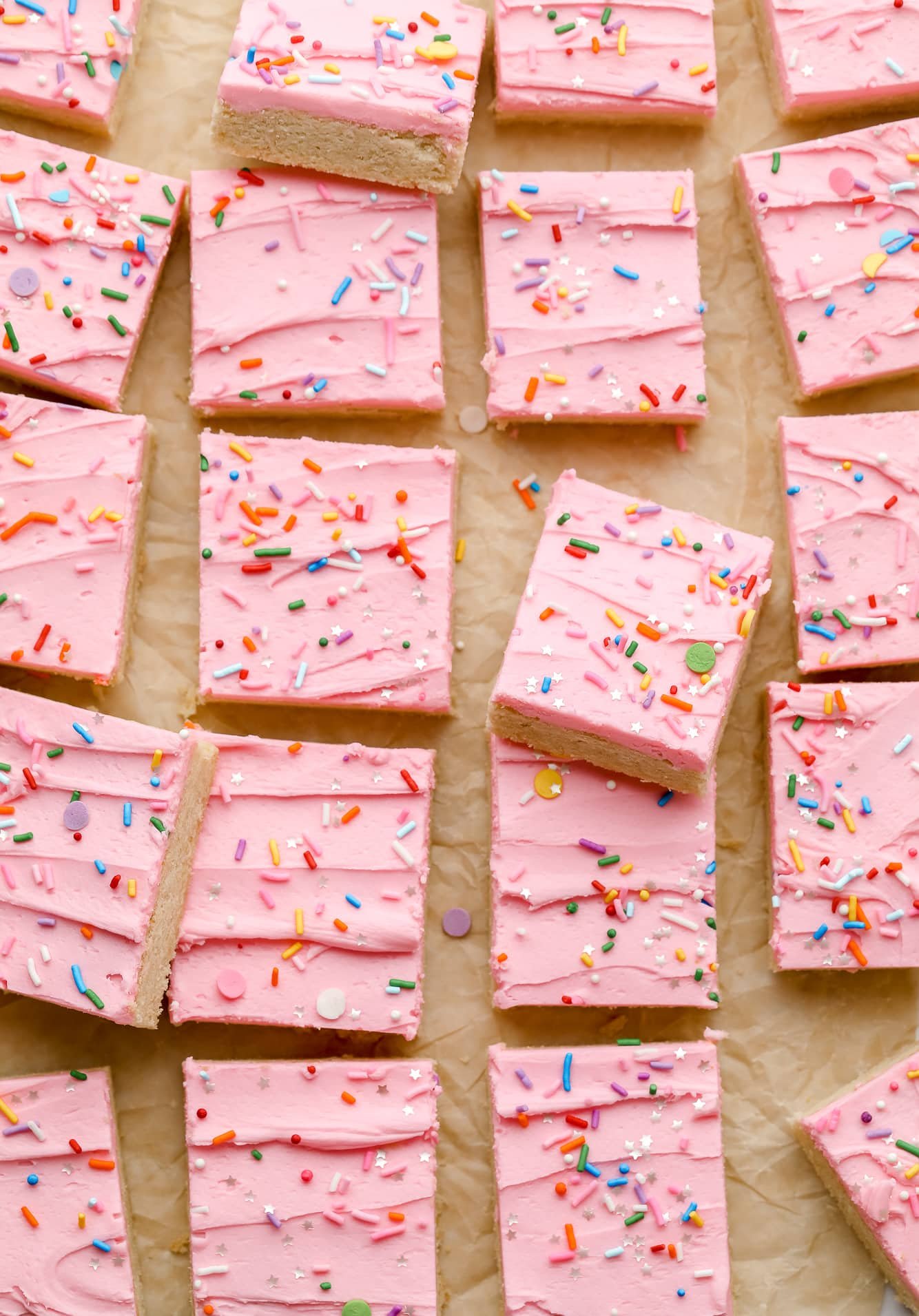 rows of sugar cookie bars decorated with pink frosting and rainbow sprinkles.
