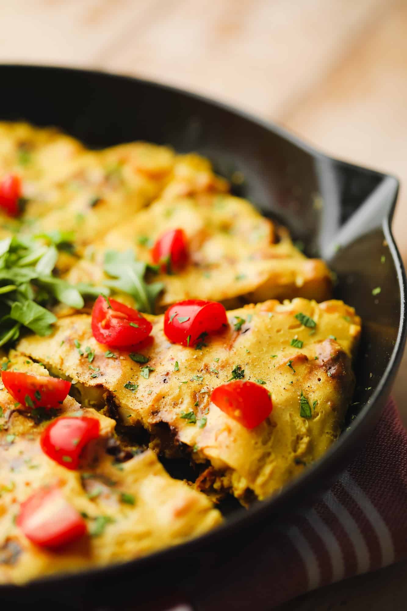 slices of a vegan frittata topped with sliced cherry tomatoes in a large black skillet.